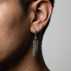 Silver feather earring worn by a person with a neutral background