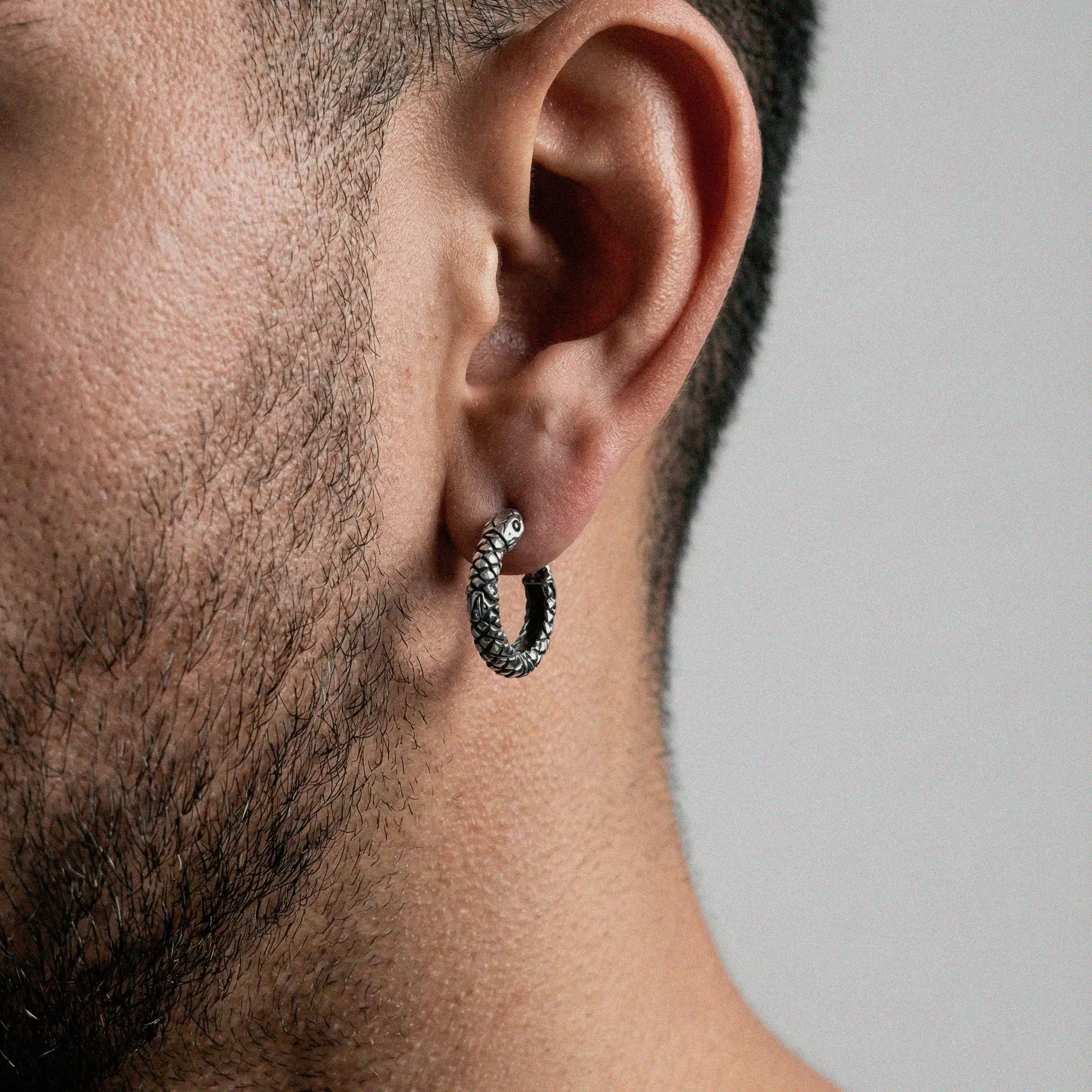 Close-up of an ear wearing a silver hoop snake earring with a blurred background