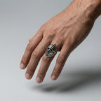 Hand wearing a silver ring with a medieval helmet design on a gray background