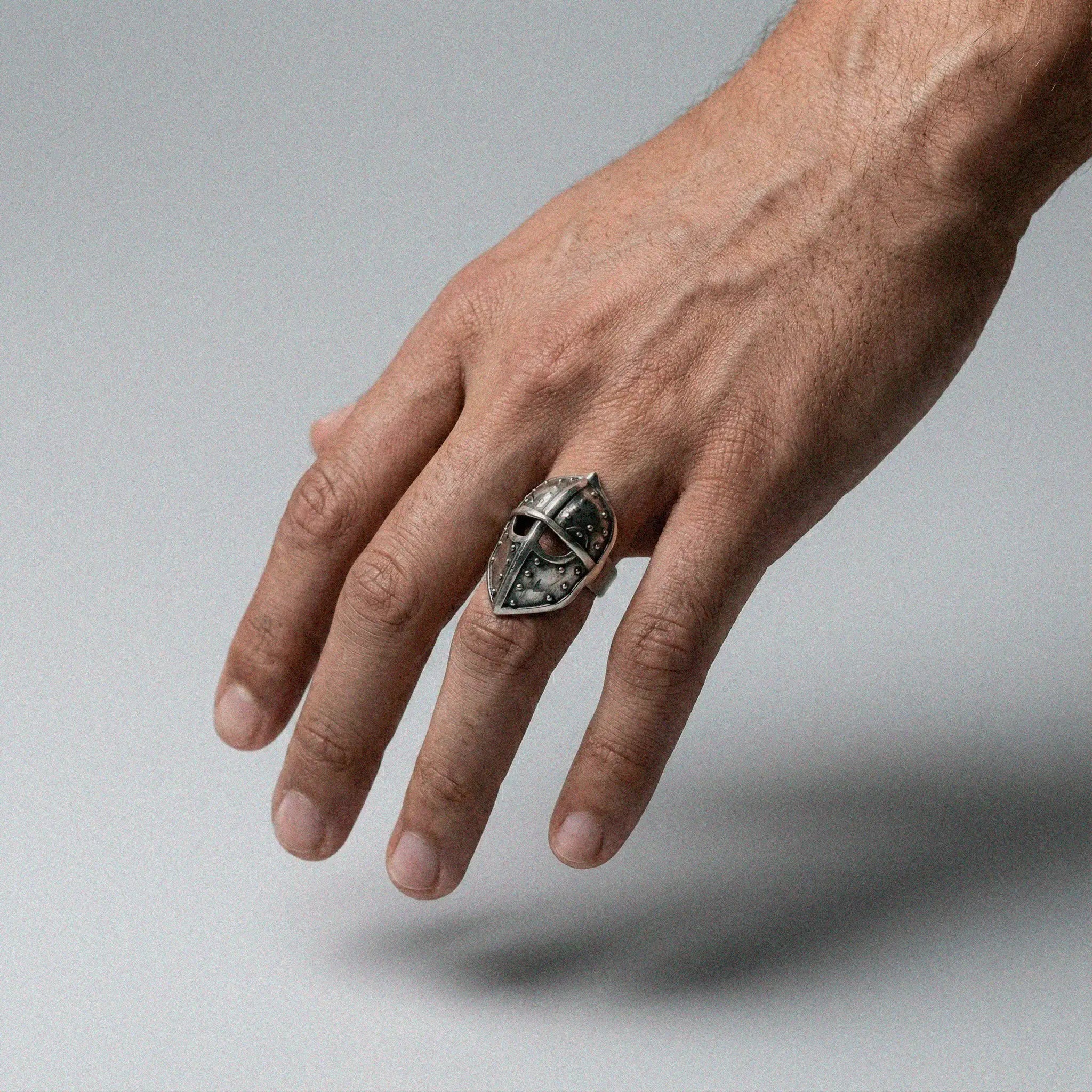 Hand wearing a silver ring with a medieval helmet design on a gray background