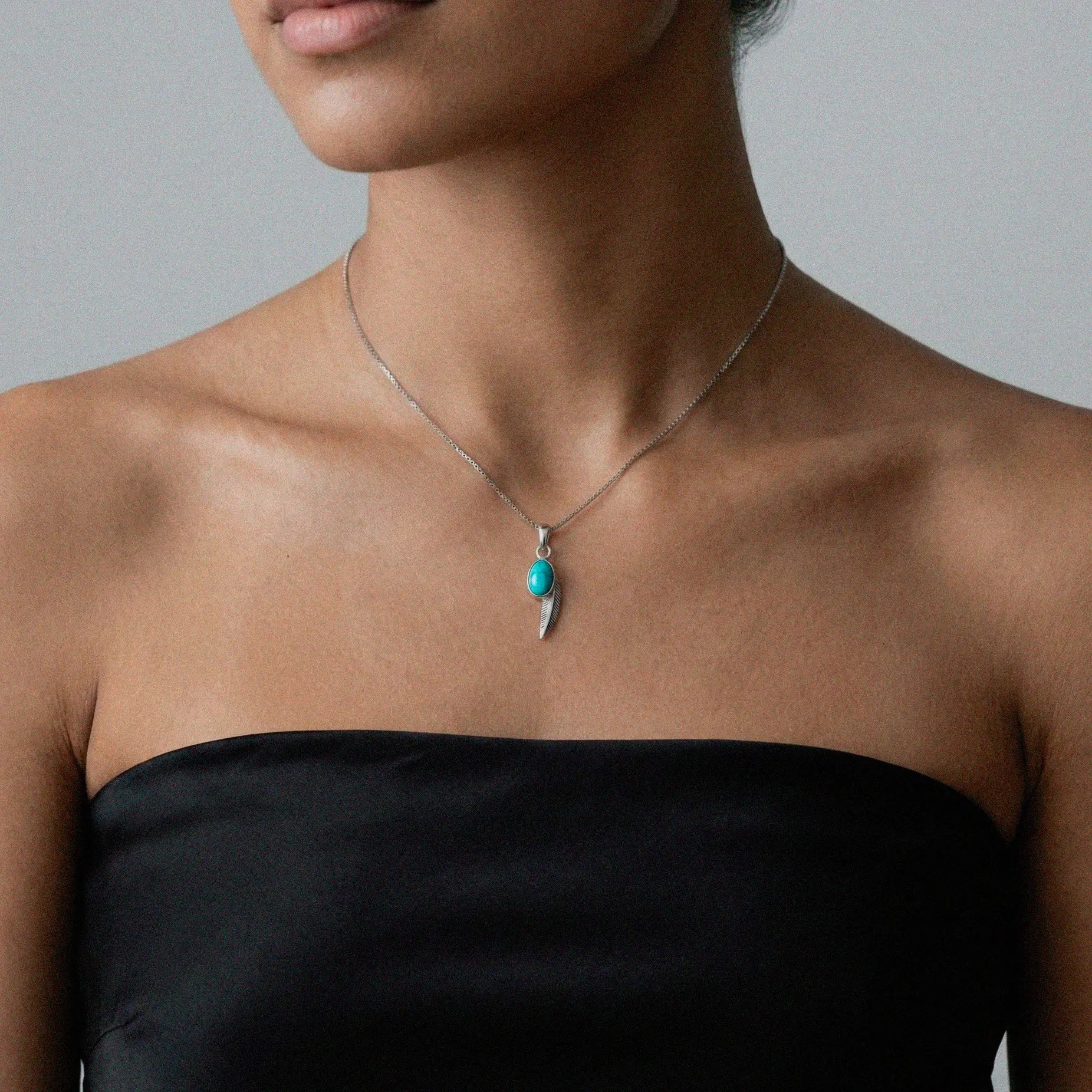 Feather necklace with a turquoise pendant worn by a person against a neutral background