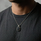 Man wearing a necklace with an obsidian pendant on a plain background
