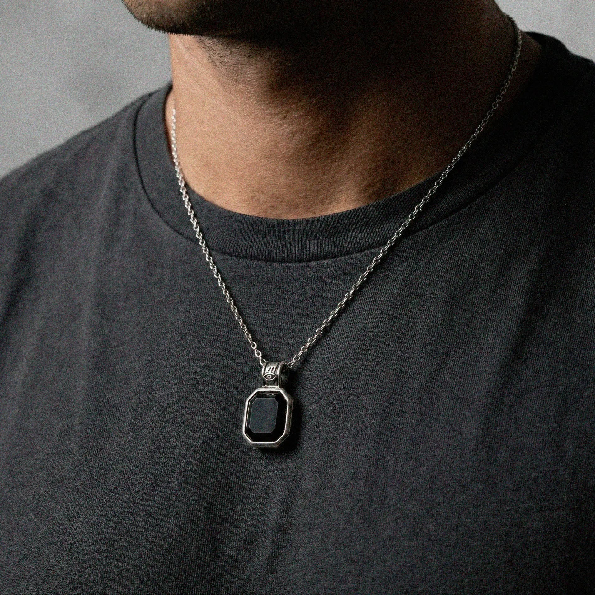 Man wearing a necklace with an obsidian pendant on a plain background