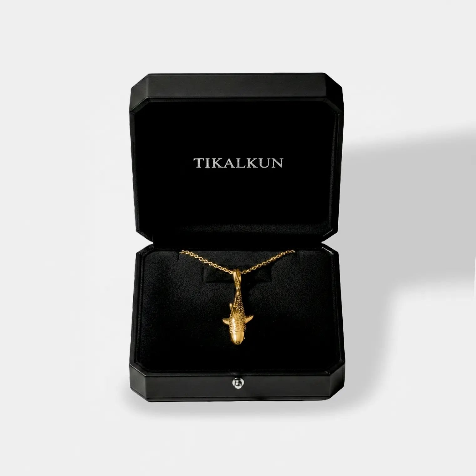 Gold tiger-shark necklace in a black Tikalkun jewelry box on a light gray background
