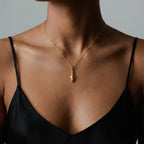 Gold tiger-shark necklace with a pendant on a person wearing a black top against a neutral background