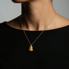 Gold tlaloc necklace with a pendant worn by a person against a neutral background