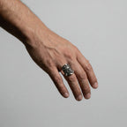 Hand wearing a silver tlaloc ring on a plain background