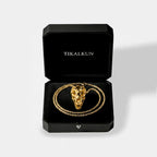 Gold necklace with t-rex skull design in a black Tikalkun box on a light gray background