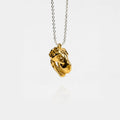 Gold dinosaur skull pendant on a silver chain against a white background