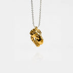 Gold dinosaur skull pendant on a silver chain against a white background