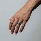 Hand wearing a silver tribal ring on a gray background