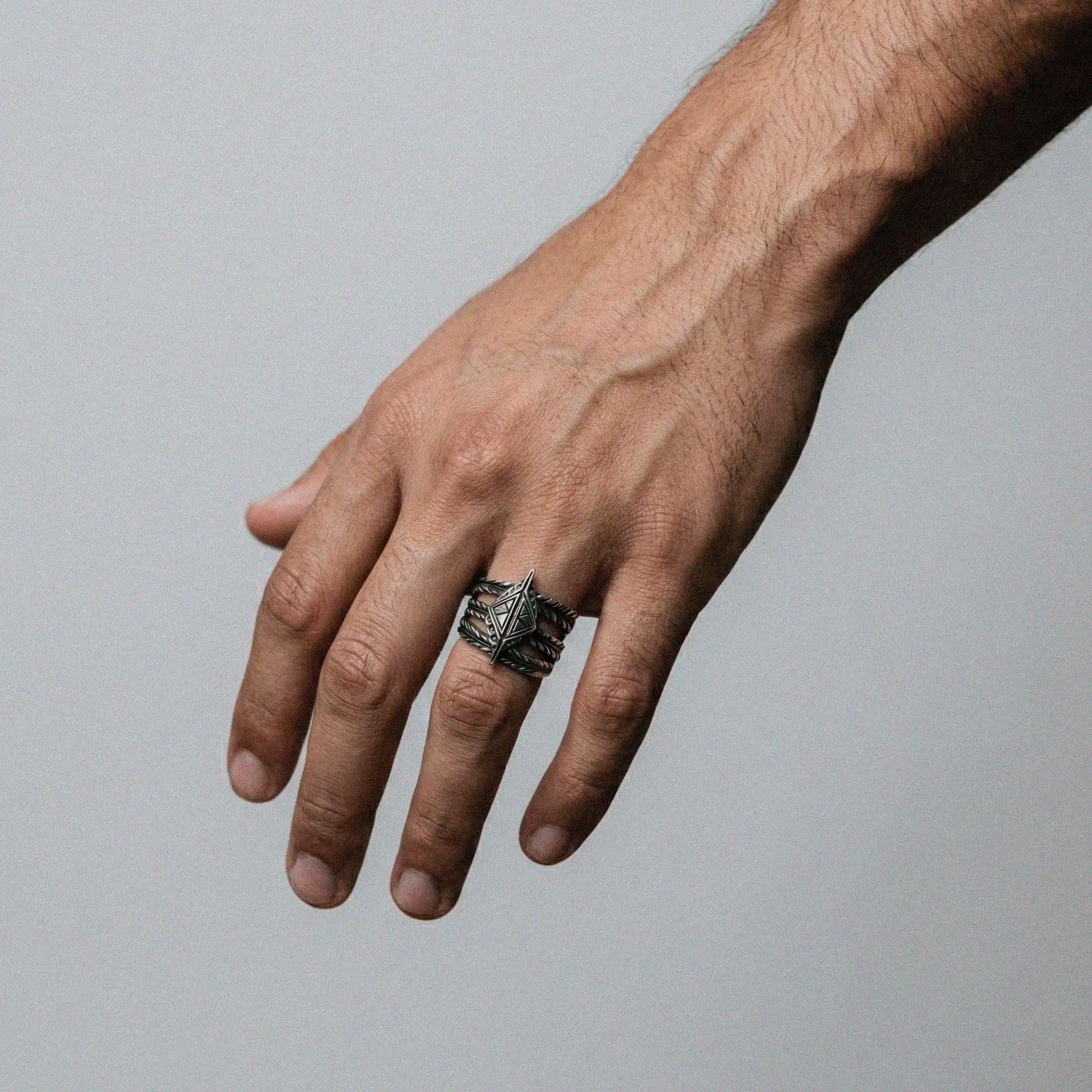 Hand wearing a silver tribal ring on a gray background