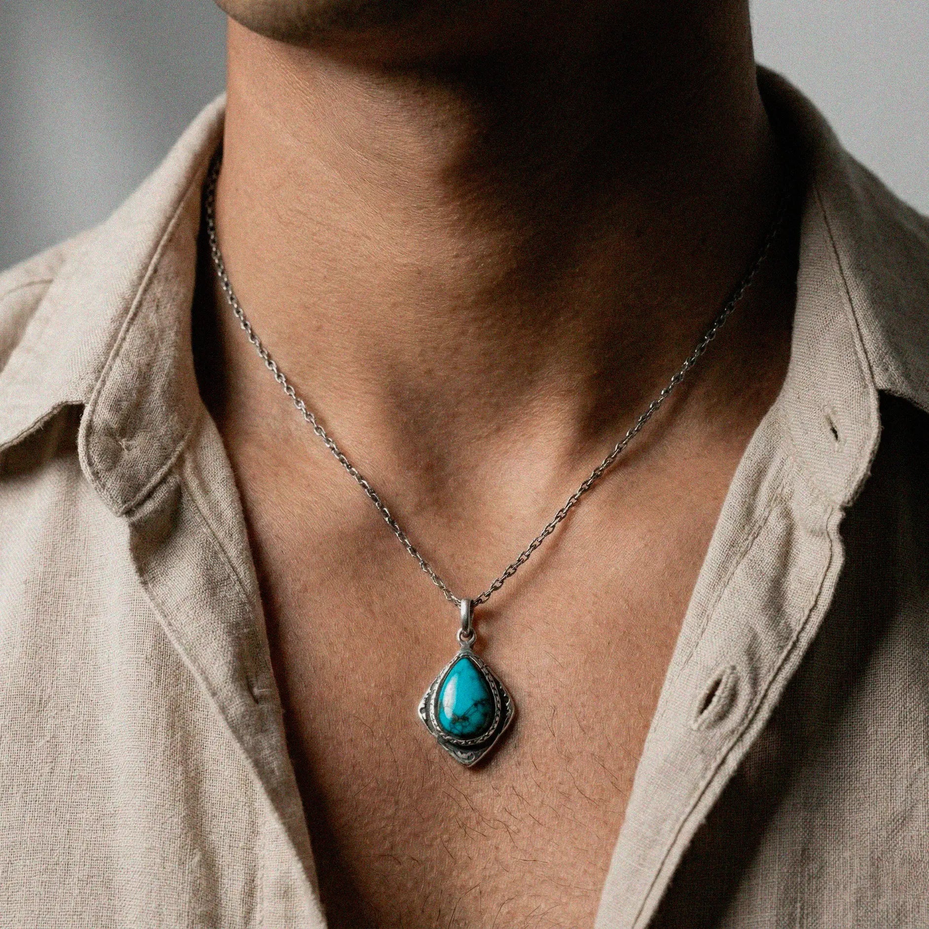 Person wearing a necklace with a turquoise pendant and beige shirt.