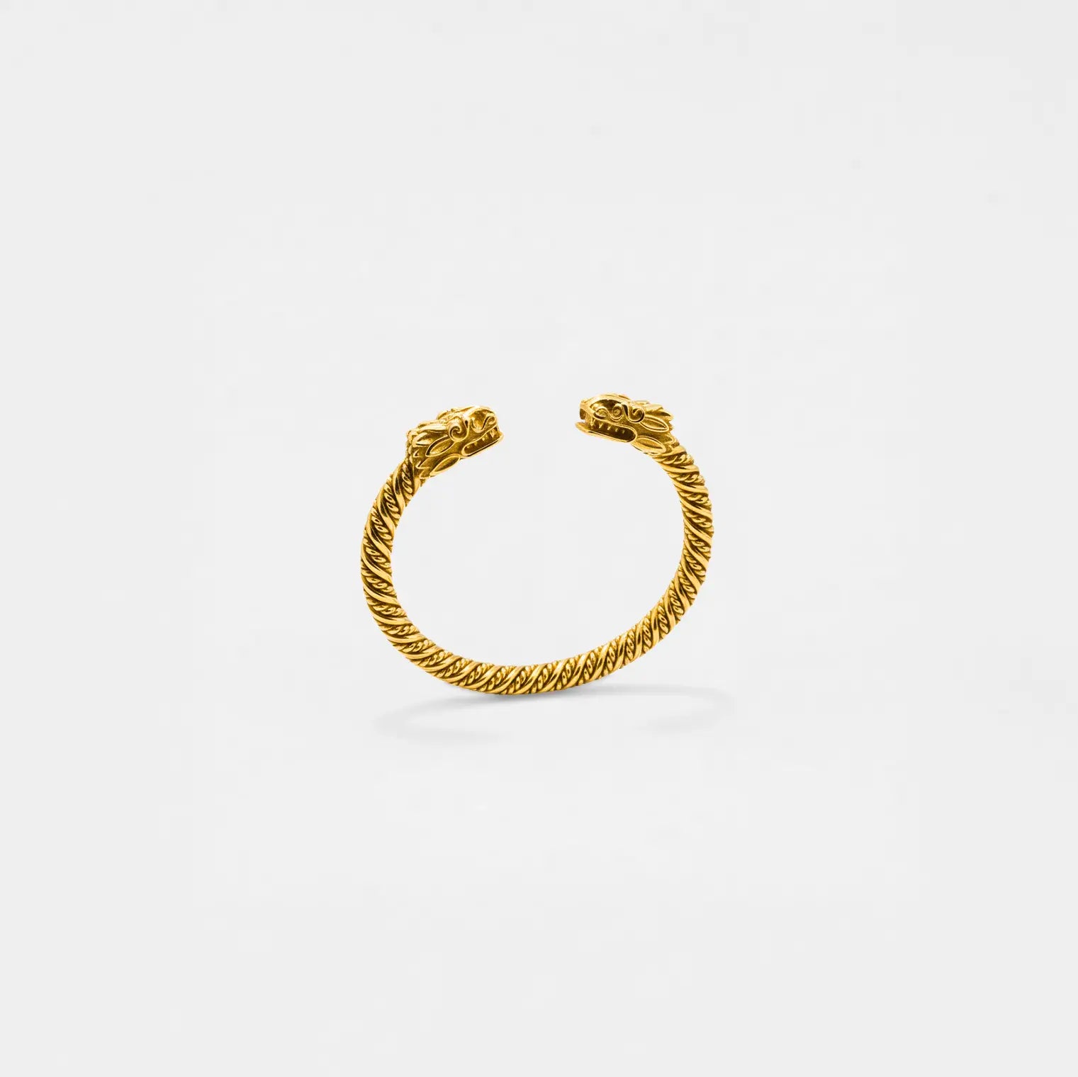 Gold quetzalcoatl bracelet on a light gray background