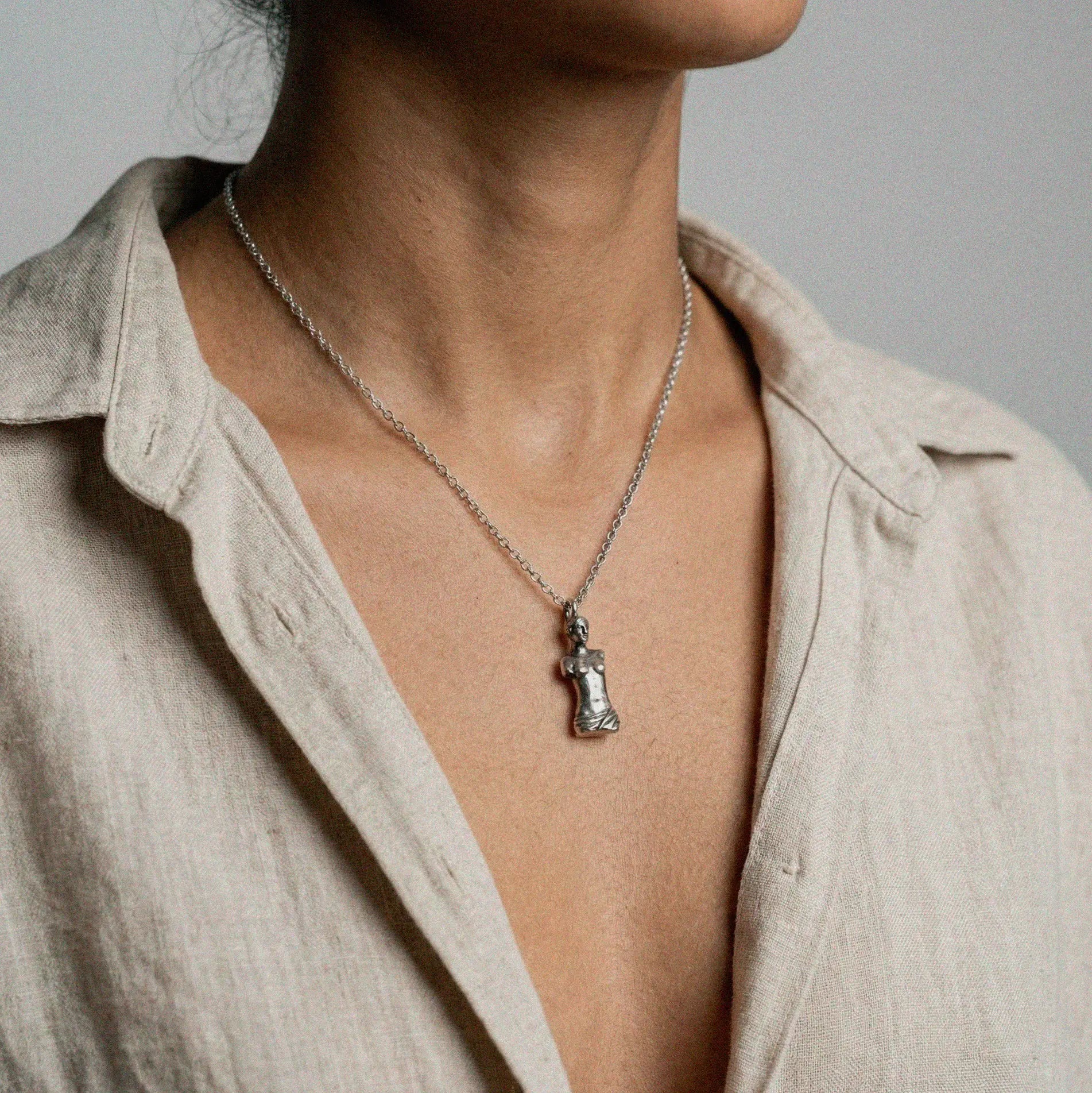 Necklace with a venus de milo pendant worn by a person against a neutral background