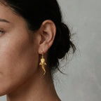 Gold whale-shark earrings worn by a person with a neutral background