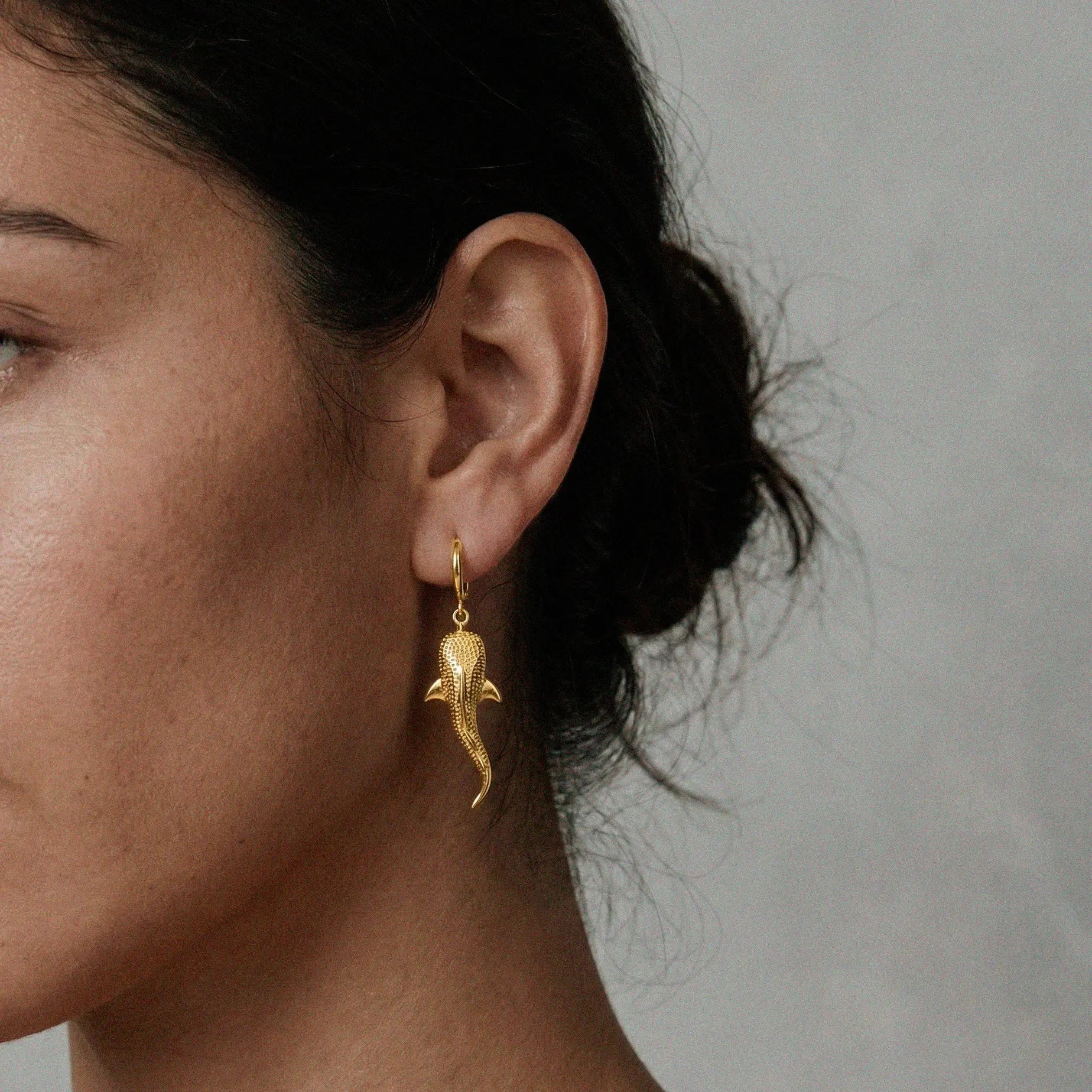 Gold whale-shark earrings worn by a person with a neutral background