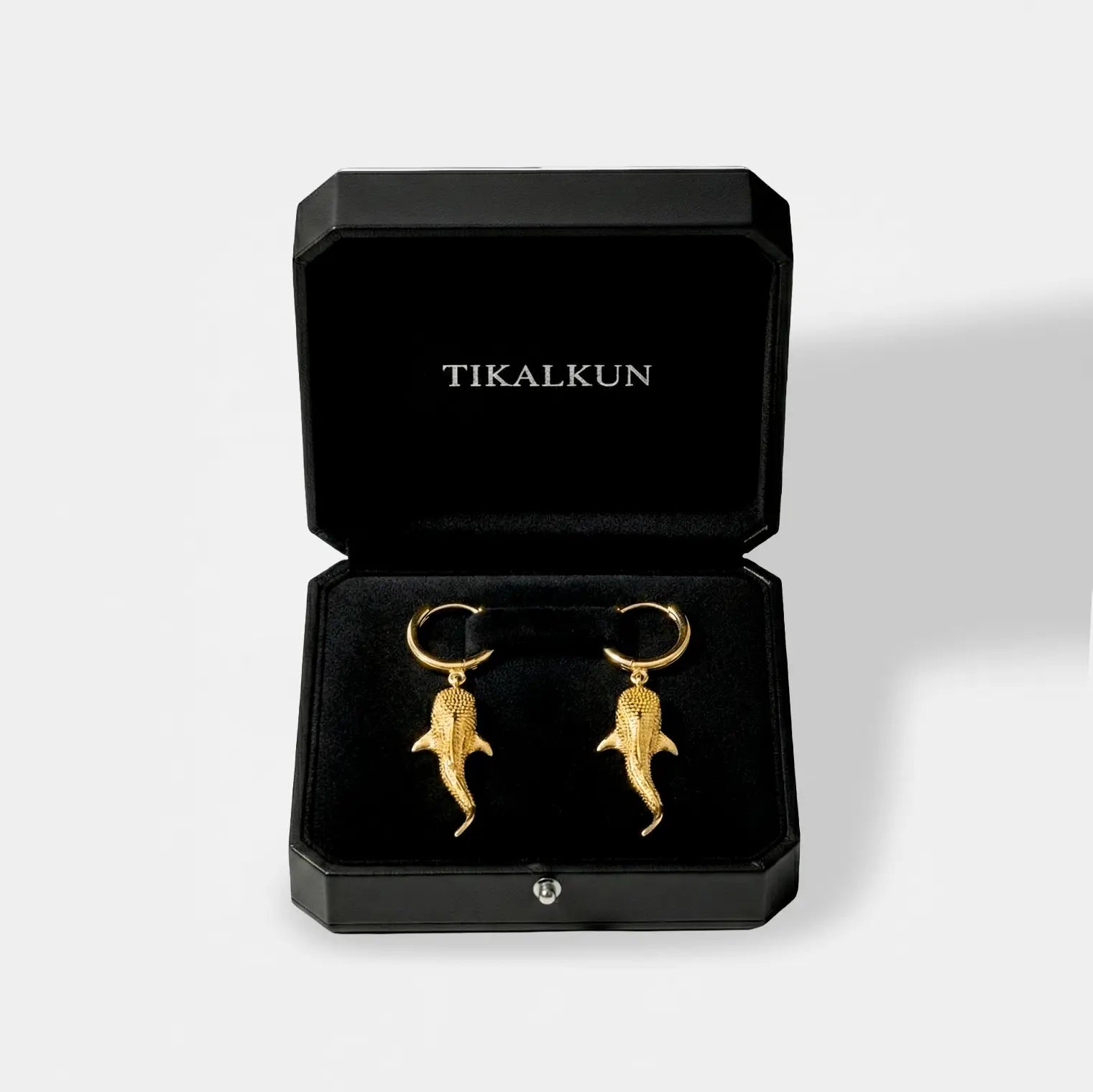 Gold whale-shark earrings in a black Tikalkun jewelry box on a light gray background