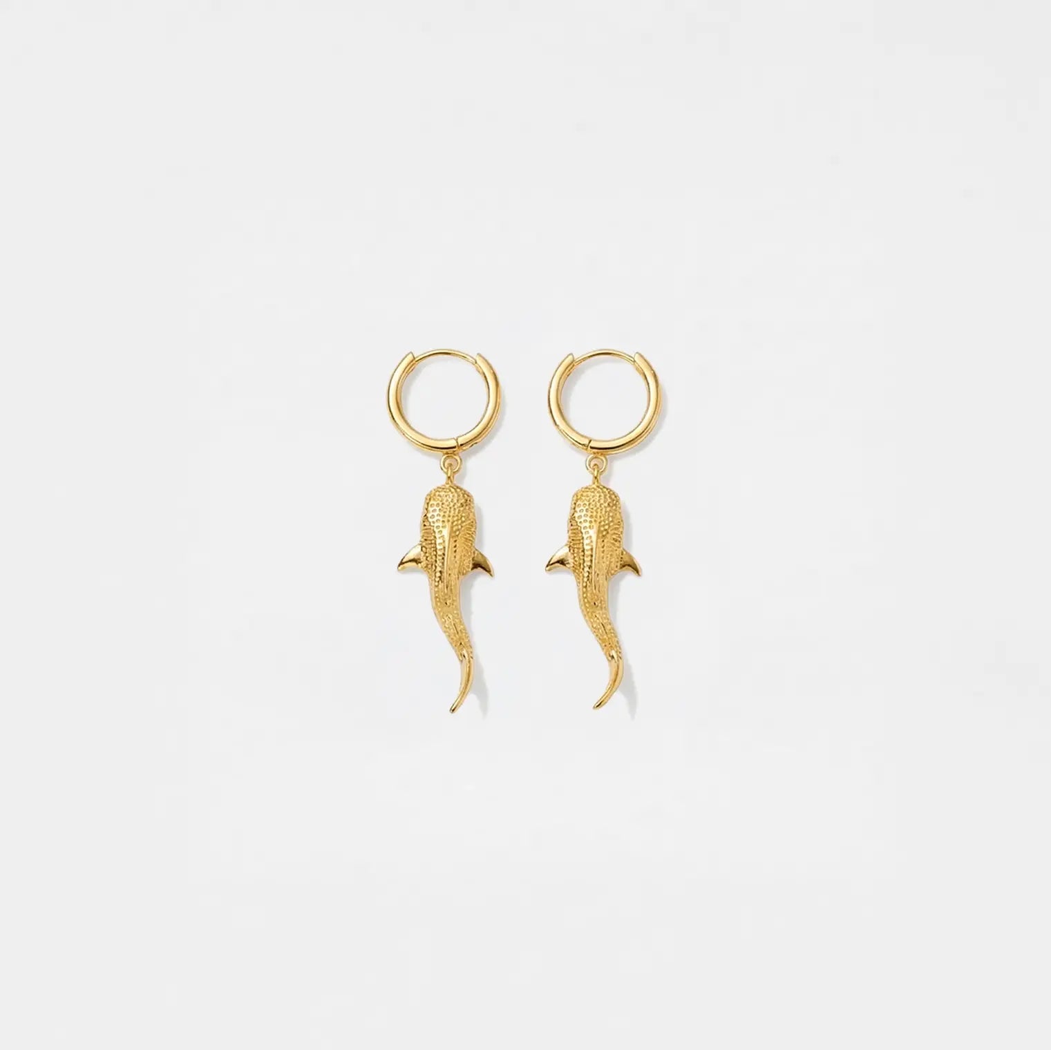 Gold whale-shark earrings on a light gray background
