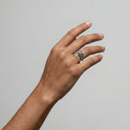 Hand wearing a silver whale-shark ring on a plain background