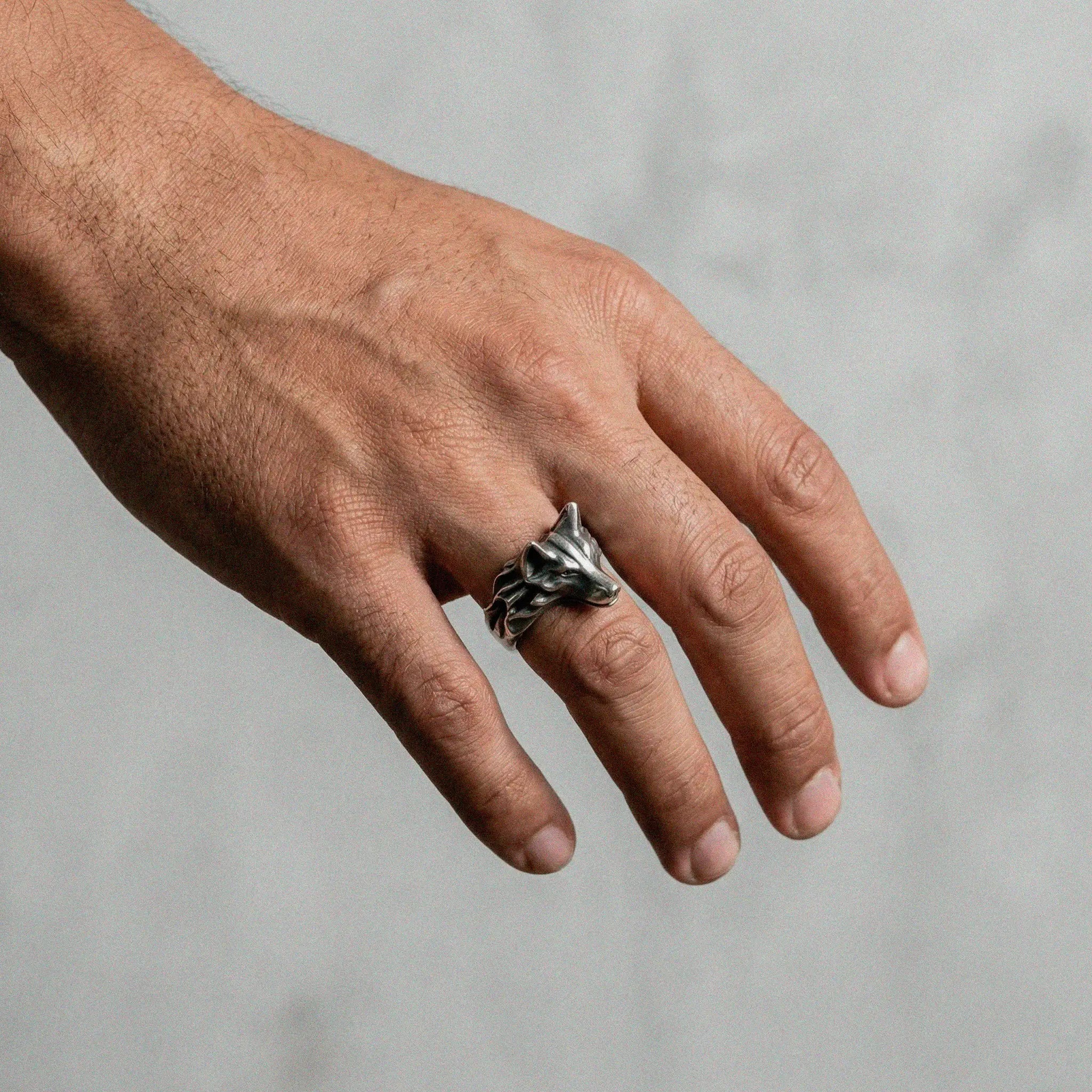 Hand wearing a silver ring with a WOLF design on a neutral background
