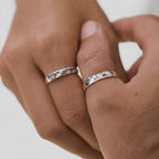 Close-up of two hands wearing matching world-map silver rings on a light background