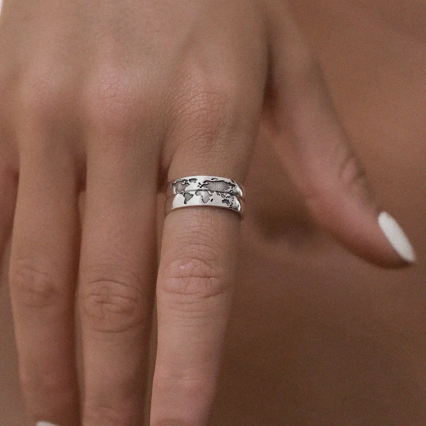 Silver ring with a world map design on a person's finger against a brown background