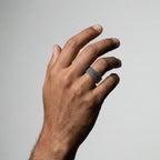 Hand wearing a patterned ring on a plain background