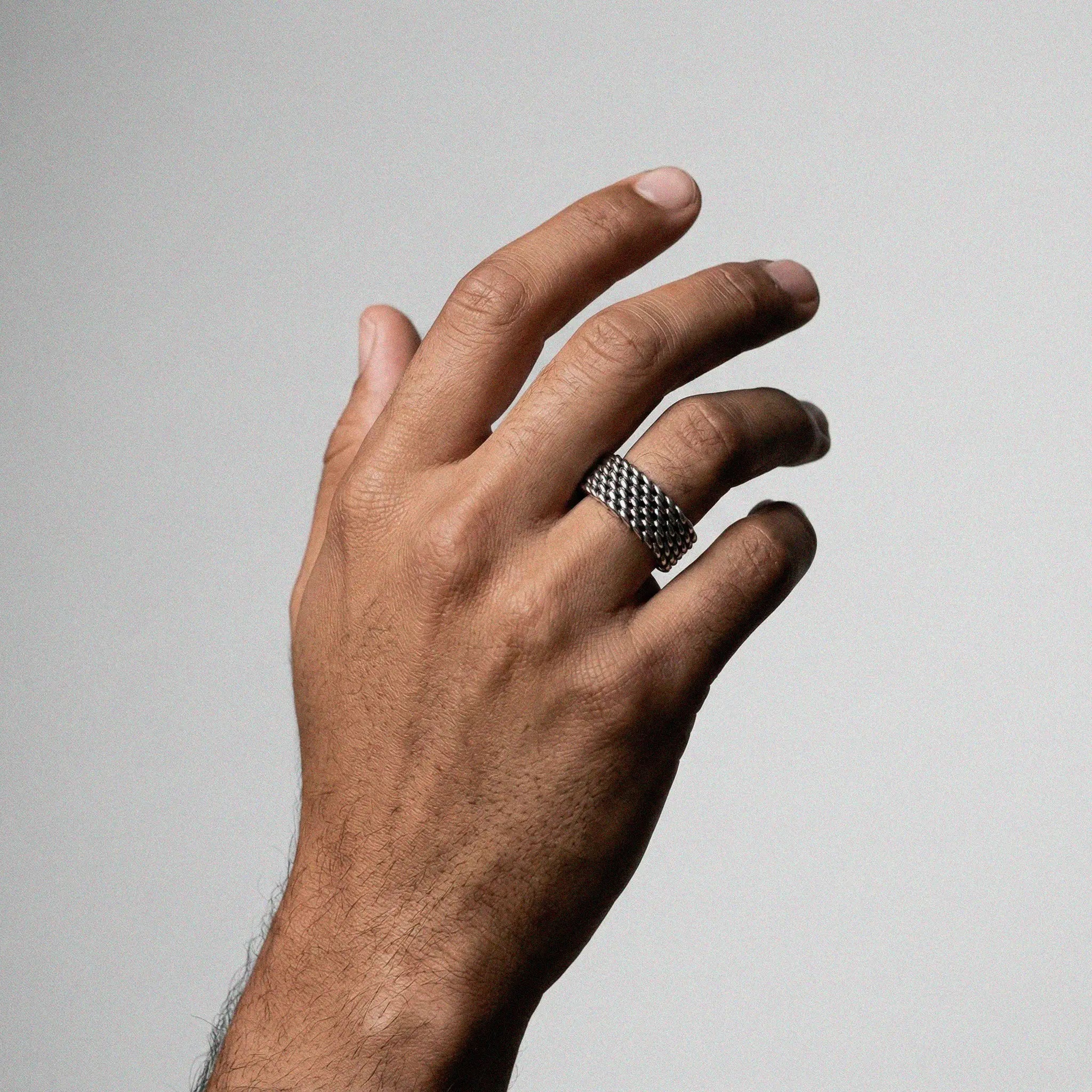 Hand wearing a patterned ring on a plain background