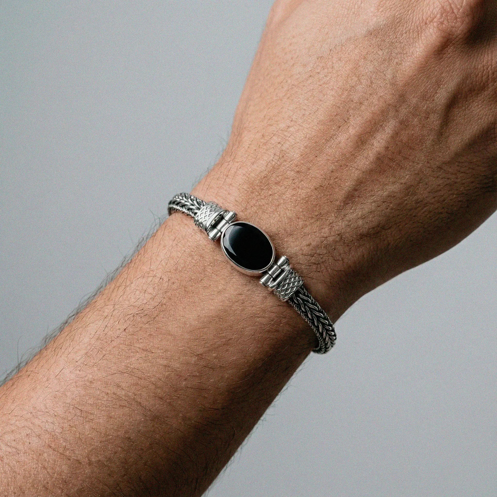 Silver bracelet with a black stone on a wrist against a gray background