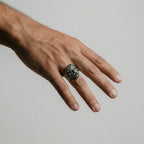 Hand wearing a silver ring with zeus design on a plain background