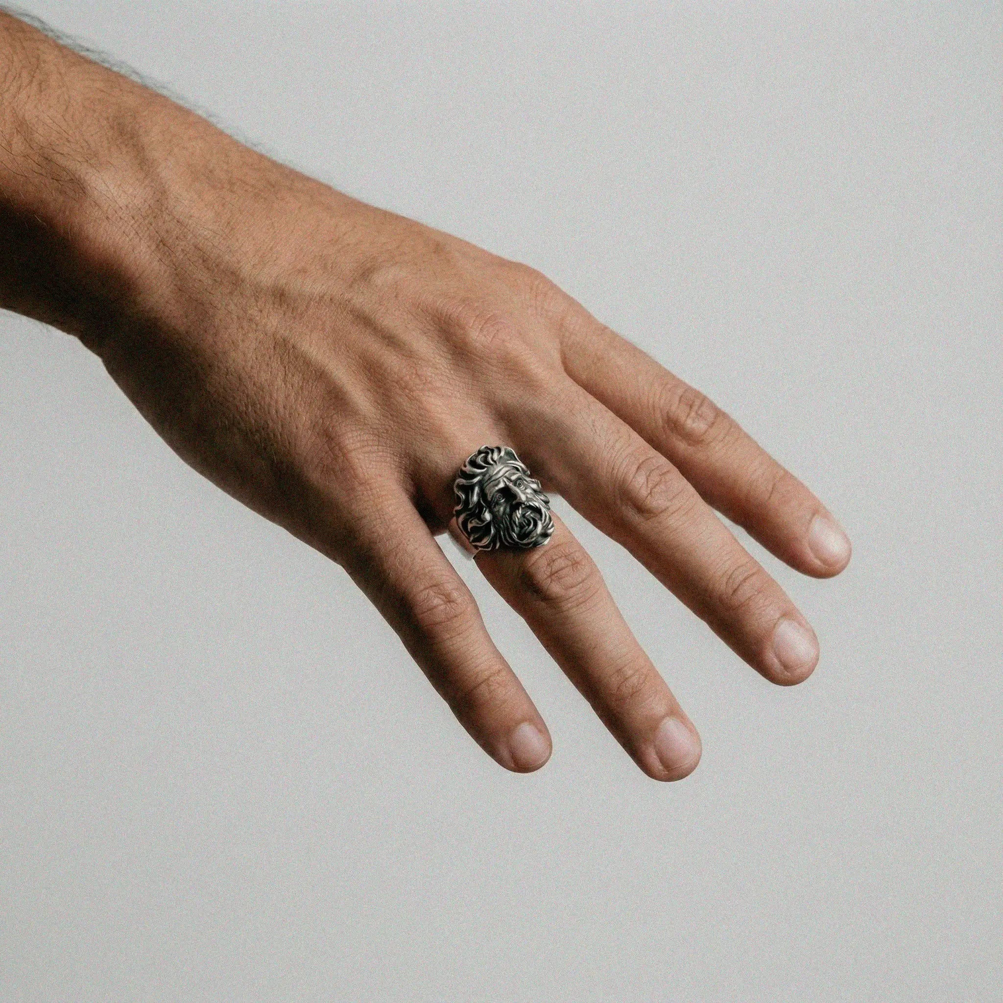 Hand wearing a silver ring with zeus design on a plain background
