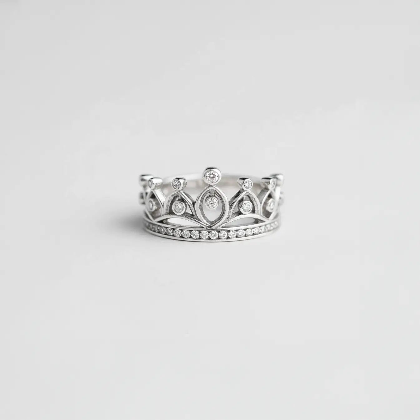 Silver crown-shaped ring with gemstones on a light gray background