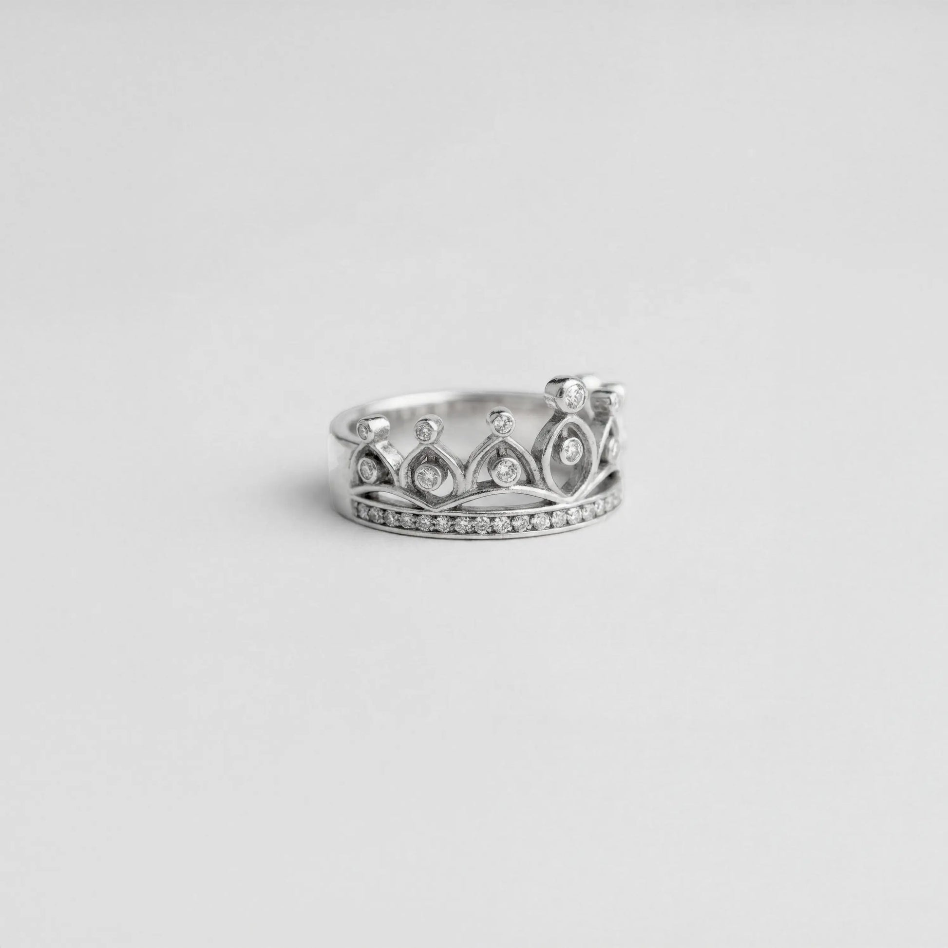 Silver crown-shaped ring with gemstones on a light gray background