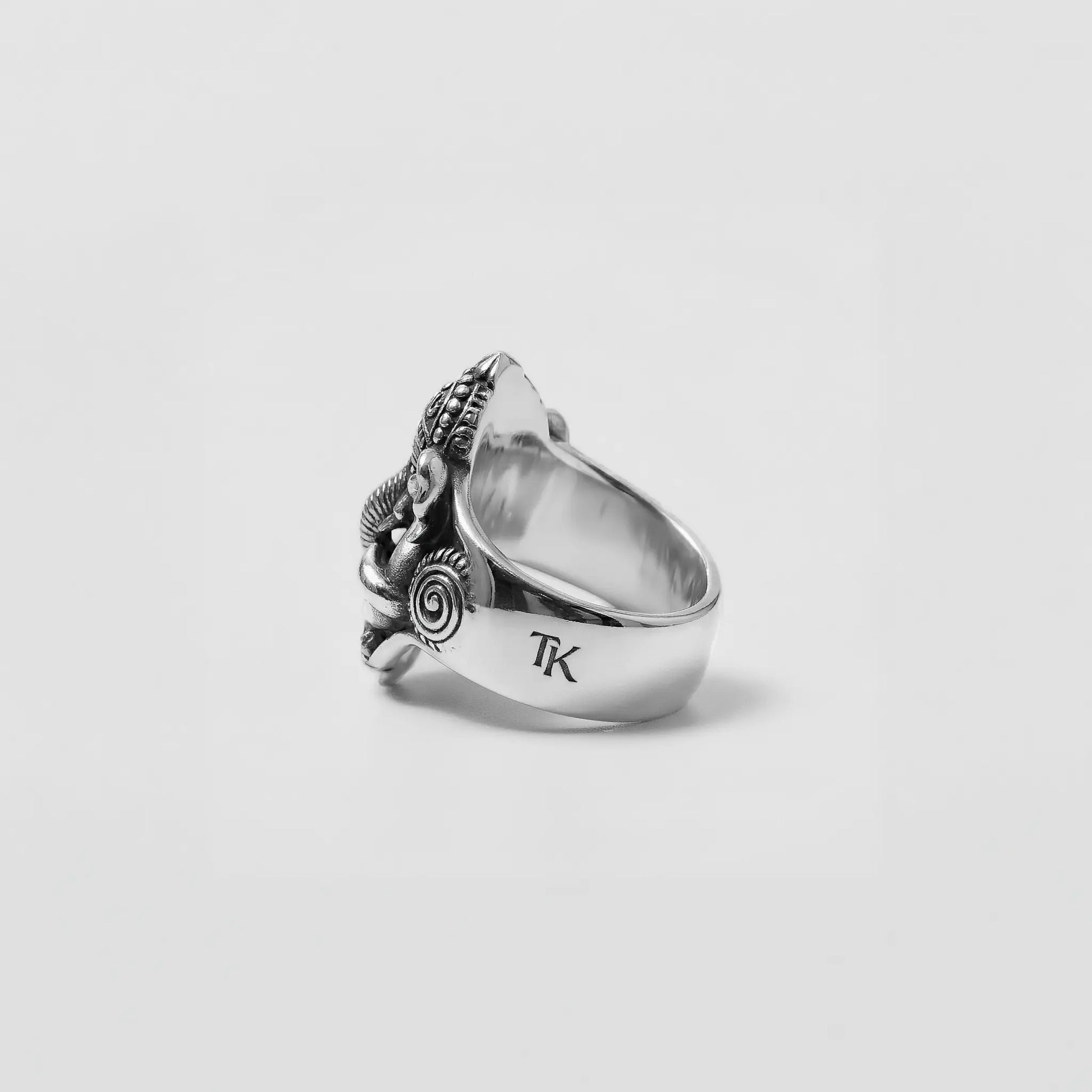Silver ring with intricate design and 'TK' initials on a light gray background
