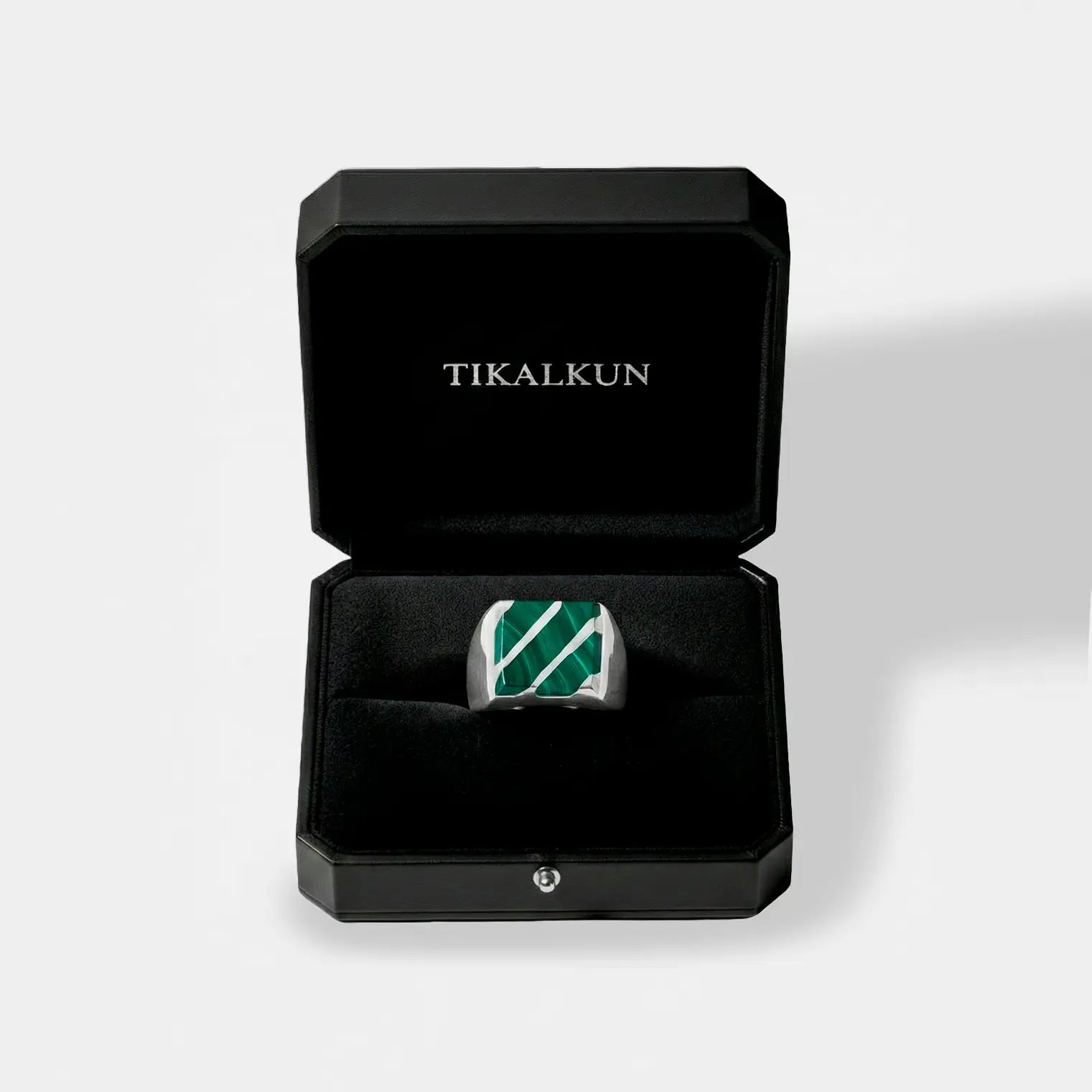 Silver ring with green stone in a black Tikalkun box on a light gray background