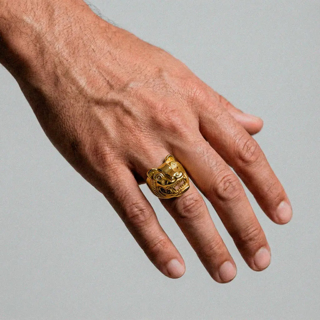 Hand wearing a gold ring with a jaguar aztec design on a plain background