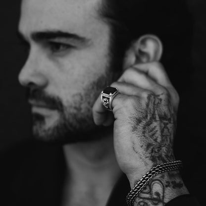 Close-up of a sterling silver laurel ring with an obsidian centerpiece worn on a tattooed hand. The intricate laurel detailing and bold black stone create a sophisticated and powerful statement piece for men.