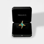 Gold lightning bolt ring with a blue gemstone in a black Tikalkun box on a light gray background