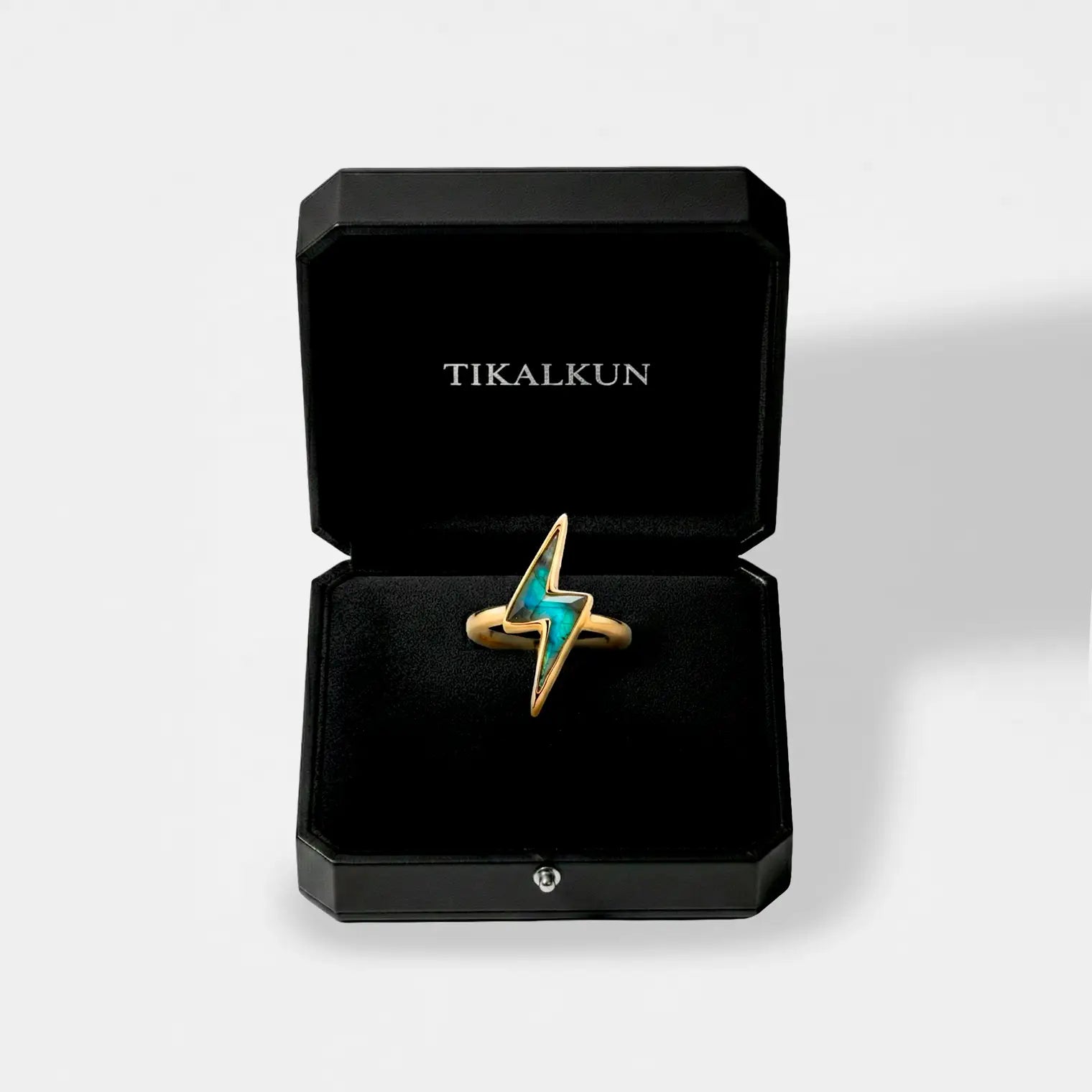 Gold lightning bolt ring with a blue gemstone in a black Tikalkun box on a light gray background