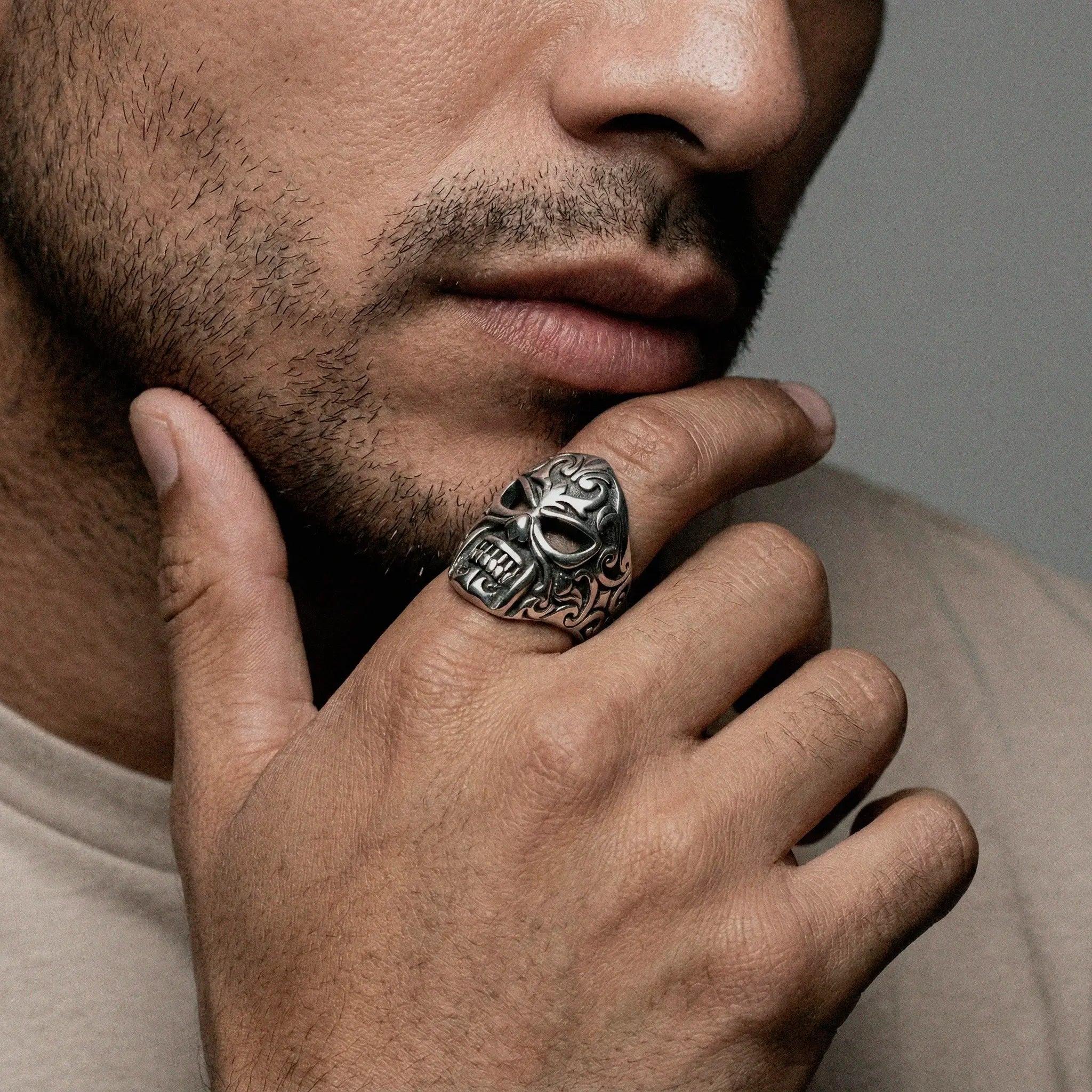 Man wearing a LUCHADOR MASK silver ring with intricate design, touching his chin.