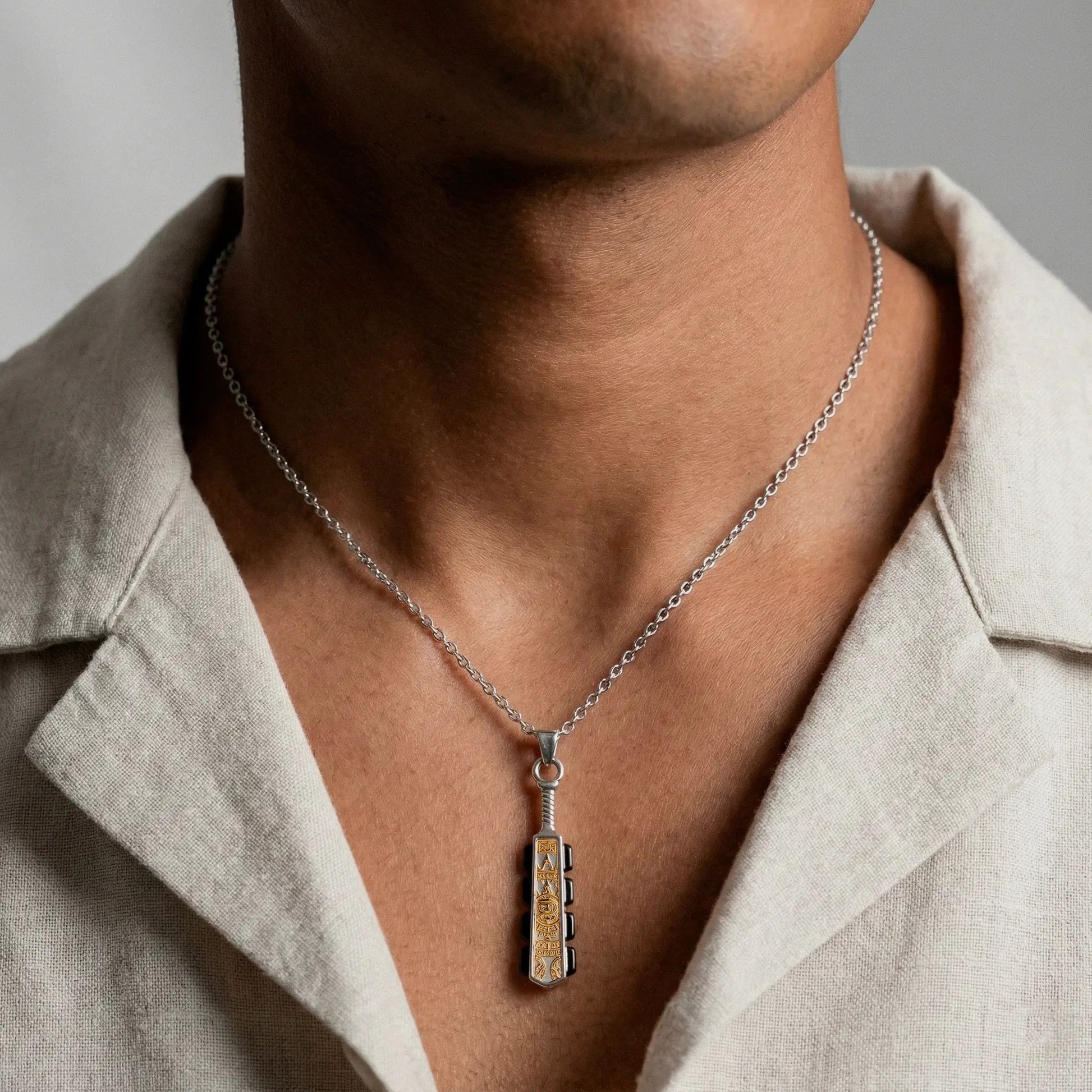 Person wearing a silver necklace with a  Necklace with a macahuitl pendant on a neutral background