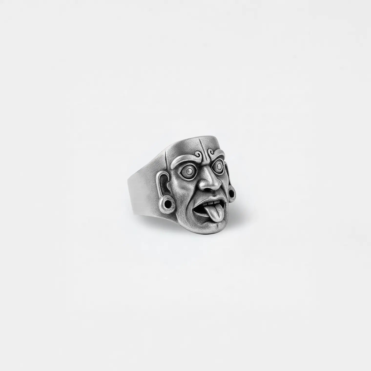 Silver mayan mask-like ring on a light gray background
