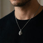 Man wearing a black shirt with a silver necklace featuring a face pendant.