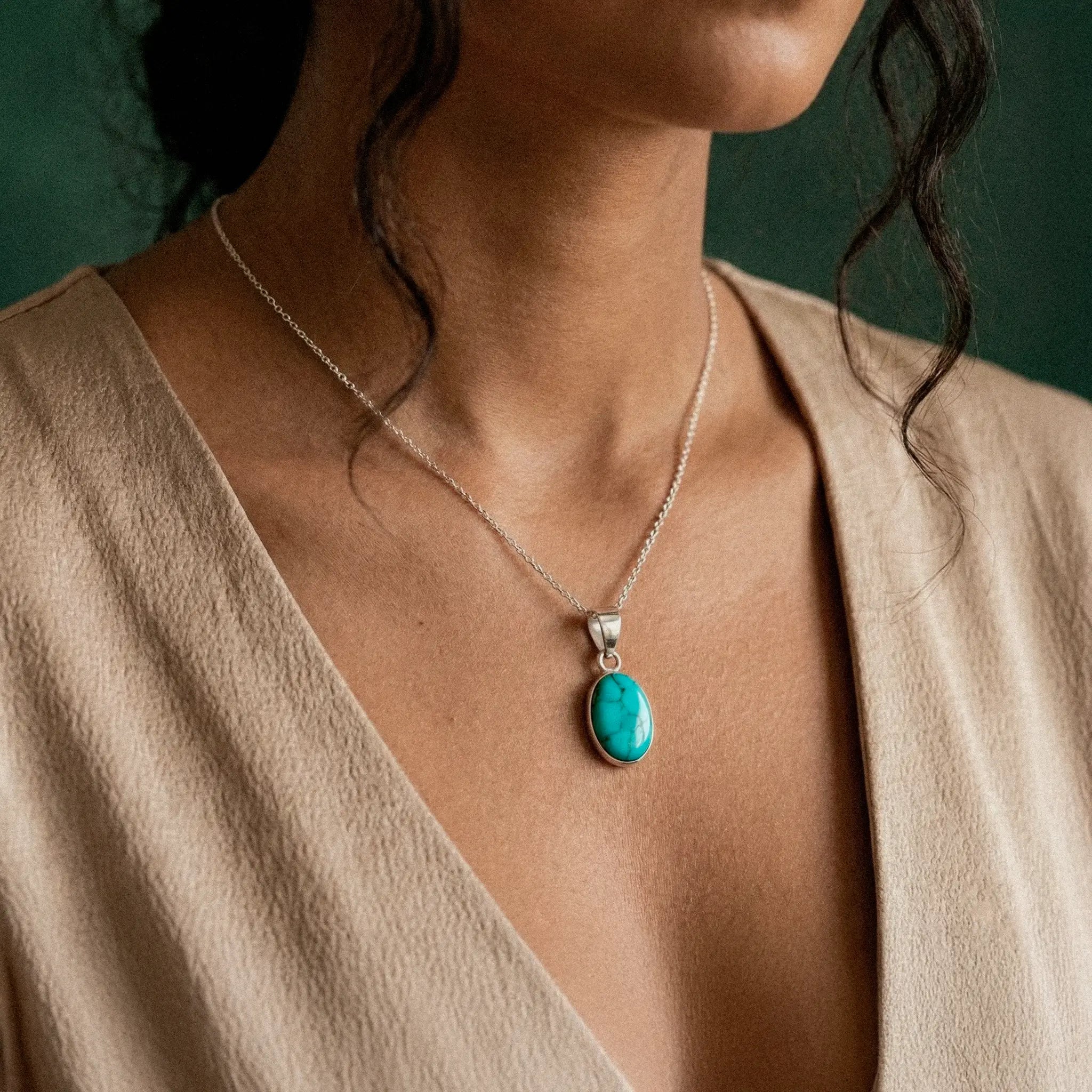 Necklace with a turquoise pendant worn by a person against a green background