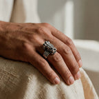 Hand wearing a silver ring with a quetzalcoatl design on a textured surface