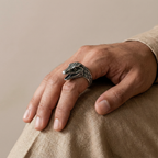 Hand wearing a silver dinosaur ring on a beige background